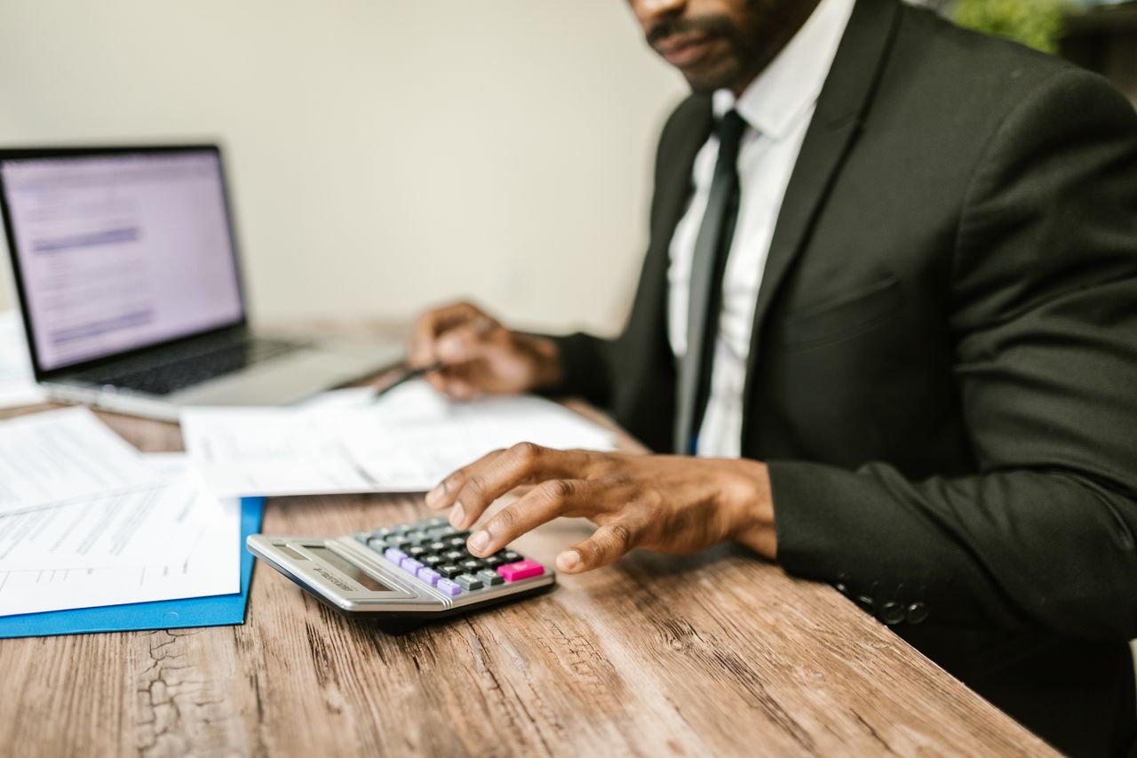 creative A businessman in a black suit using a calculator at a desk with financial documents and a laptop.